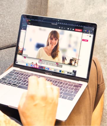 Ein Laptop auf dem Schoß. Darauf ist eine Videokonferenz mit einer Kollegin zu sehen.